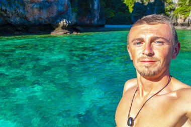 Turist erkek adam, kireçtaşından kayalar ve turkuaz mavi su Koh Phi Phi Leh adası Ao Nang Krabi Tayland arasındaki ünlü plaj gölünde selfie çekiyor..