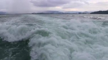 Feribotla uzun kuyruklu yat ve yüksek dalgalarla turkuvaz su plajındaki tropikal manzara manzarası boyunca Phuket adası Tayland 'daki Ratsada Amphoe Mueang Phuket' teki kireçtaşı kayaları arasında seyahat edin..