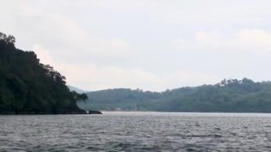 Feribotla uzun kuyruklu yat ve yüksek dalgalarla turkuvaz su plajındaki tropikal manzara manzarası boyunca Phuket adası Tayland 'daki Ratsada Amphoe Mueang Phuket' teki kireçtaşı kayaları arasında seyahat edin..