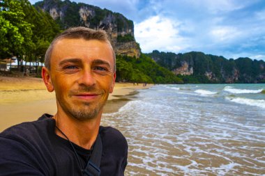 Genç yakışıklı adam tropik cennet manzaralı turkuaz su plajında ve Ao Nang Krabi Tayland 'daki Ao Nang Sahili' ndeki kireçtaşı kayalıkları arasında selfie çekiyor..
