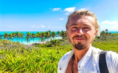 Yakışıklı erkek turist erkek gezgin muhteşem manzara manzarası turkuvaz mavi palmiye ağaçları mavi gökyüzü tropikal plaj ve ormanlar güzel Meksika adası Contoy.