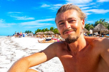 Yakışıklı erkek turist, güzel Holbox adası kumsalında ve Meksika 'da turkuvaz suyu ve mavi gökyüzü olan kumsalda manzara manzaralı selfie çekiyor..