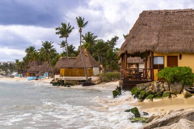 Tropik Meksika Karayip plajı ve denizi kulübeleriyle kulübeleriyle çatı palapa güneşiyle güneşleniyor güneş şemsiyeleriyle turkuaz su otelleri Playa del Carmen Meksika 'da tatil yapıyor..