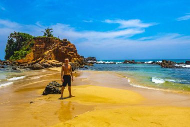 Genç yakışıklı erkek turist papağan kayasında tropik cennet kumsalında Mirissa Beach Matara Bölgesi Güney Sri Lanka Bölgesi 'nde turkuaz suyla.