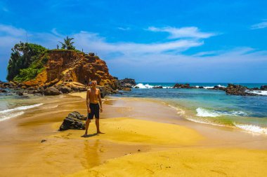 Genç yakışıklı erkek turist papağan kayasında tropik cennet kumsalında Mirissa Beach Matara Bölgesi Güney Sri Lanka Bölgesi 'nde turkuaz suyla.