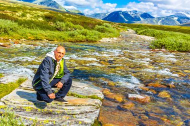 Young hiker and beautiful summer landscape panorama with mountains river lake rocks and hiking trail of Rondane National Park in Ringbu Innlandet Norway in Scandinavia. clipart