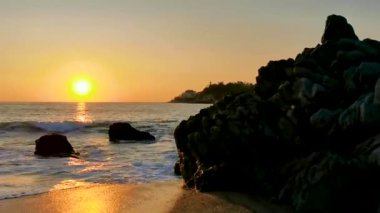 Güzel, göz kamaştırıcı, renkli ve altın sarısı günbatımı. Plajda sarı turuncu kırmızı ve büyük bir sörfçü dalgası ve kayalıklar. Zicatela Puerto Escondido Oaxaca Meksika 'da tropikal doğada uçurum manzarası..