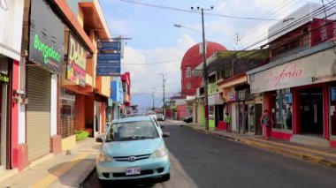 Trafik kaldırımları olan tipik cadde araba mağazaları ve Orta Amerika Alajuela Kosta Rika 'daki insanlar.