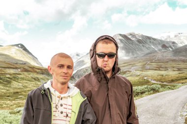 Young male hiker men friends and beautiful summer landscape panorama with mountains river lake rocks and hiking trail of Rondane National Park in Ringbu Innlandet Norway in Scandinavia. clipart