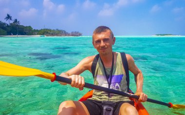 Male tourist man with canoe boat has fun sport kayaking in turquoise clear water and tropical nature on Rasdhoo island in Rasdhoo Atoll Maldives. clipart