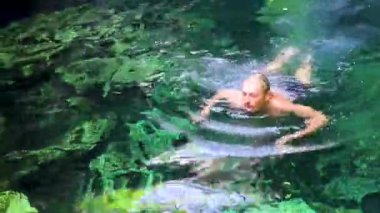 Erkek turist, Xpu Ha Quintana Roo Meksika 'da Cenote Park Minotauro' nun turkuaz mavi sularında kireç taşı kayaları ve doğa ormanıyla yüzüyor..