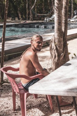 Man male tourist relax relaxing in the tropical jungle and nature with limestone rocks palm trees and plants of the Cenote Park Minotauro in Xpu Ha Quintana Roo Mexico. clipart