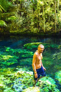Erkek turist, Xpu Ha Quintana Roo Meksika 'da Cenote Park Minotauro' nun turkuaz mavi sularında kireç taşı kayaları ve doğa ormanıyla yüzüyor..