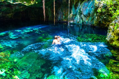 Erkek turist, Xpu Ha Quintana Roo Meksika 'da Cenote Park Minotauro' nun turkuaz mavi sularında kireç taşı kayaları ve doğa ormanıyla yüzüyor..