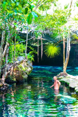 Erkek turist, Xpu Ha Quintana Roo Meksika 'da Cenote Park Minotauro' nun turkuaz mavi sularında kireç taşı kayaları ve doğa ormanıyla yüzüyor..