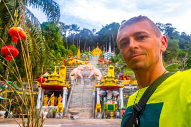 Handsome male tourist traveler man takes selfie photo at Wat Phu Khao Phra Maha Phothisat Chinese temple on the hill in Ao Nang Amphoe Mueang Krabi Thailand. clipart