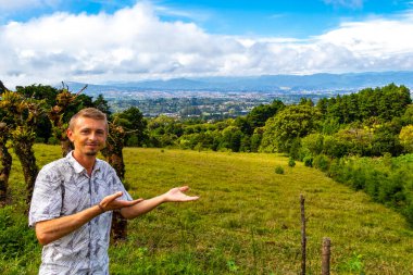 Handsome man male tourist with beautiful mountain landscape and panorama with forest trees clouds and nature of San Jose and Heredia Costa Rica in Central America. clipart