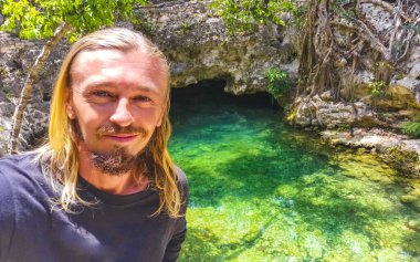 Erkek tur rehberi, Tulum Quintana Roo Mexico 'daki Yaxmuul mezarlığında turkuaz yeşil su ve kayalarda poz veriyor..