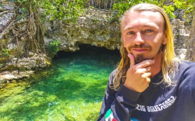 Erkek tur rehberi, Tulum Quintana Roo Mexico 'daki Yaxmuul mezarlığında turkuaz yeşil su ve kayalarda poz veriyor..