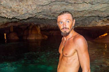 Erkek tur rehberi, Tulum Quintana Roo Mexico 'daki Yaxmulito mezarlığında turkuaz yeşil su ve kayalarda poz veriyor..