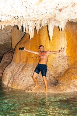Erkek tur rehberi, Tulum Quintana Roo Mexico 'daki Yaxmulito mezarlığında turkuaz yeşil su ve kayalarda poz veriyor..