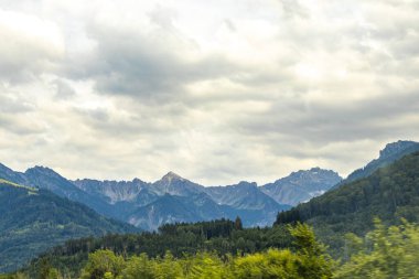 Dağ manzarası dağları yeşil tarlalar orman bulutları ve mavi gökyüzü Alpler Vorarlberg Avusturya.