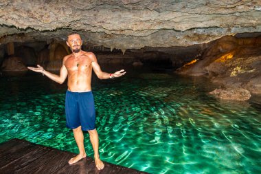 Erkek tur rehberi, Tulum Quintana Roo Mexico 'daki Yaxmulito mezarlığında turkuaz yeşil su ve kayalarda poz veriyor..