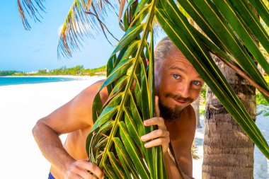 Uzun saçlı erkek turist, Meksika 'nın Playa del Carmen Quintana Roo Meksika sahilindeki bir hindistan cevizi ağacında fotoğraf mankeni için poz veriyor..