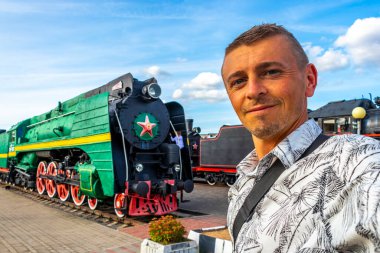 Klasik antika antika trenli yakışıklı erkek turist Leninskiy Rayon Brest Belarus 'taki Demiryolu Mühendislik Müzesi' nde buharlı lokomotifler eğitiyor..