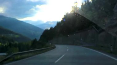 Yeşil tarlalar, orman bulutları, arabalar ve Alpler 'deki mavi gökyüzü ile otoyol üzerindeki bir dağ manzarası dağları boyunca sürüyorum..