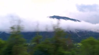 Yeşil tarlalar, orman bulutları, arabalar ve Alpler Vorarlberg Avusturya 'da mavi gökyüzü olan bir dağ manzarası boyunca sürüş yapmak..