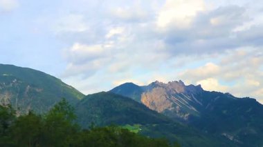 Yeşil tarlalar, orman bulutları, arabalar ve Alpler Vorarlberg Avusturya 'da mavi gökyüzü olan bir dağ manzarası boyunca sürüş yapmak..