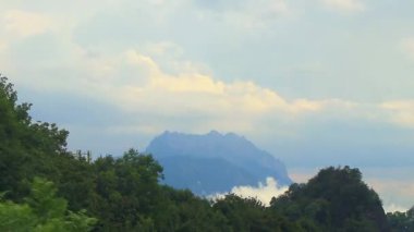 Yeşil tarlalar, orman bulutları, arabalar ve Alpler Vorarlberg Avusturya 'da mavi gökyüzü olan bir dağ manzarası boyunca sürüş yapmak..