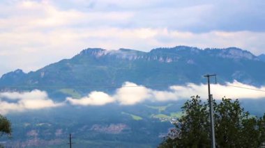 Dağ ve dağlık arazi dağları ve yeşil tarlalı zirveler orman bulutları ve Alpler 'deki mavi gökyüzü Vorarlberg Avusturya.