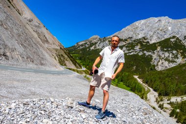 Dağlarda ve Alp Dağları 'nda kamerası olan yakışıklı bir turist. Dağlar, kayalar, orman köknar ağaçları ve Alpler' de mavi gökyüzü olan manzaralar..