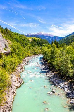 Turkuaz mavi ve yeşil nehir buharı ve köprü taşlı şelale hanı. Çimen ağaçları, doğa ve dağ manzarası. Alplerde uçan Landeck Tyrol Avusturya..