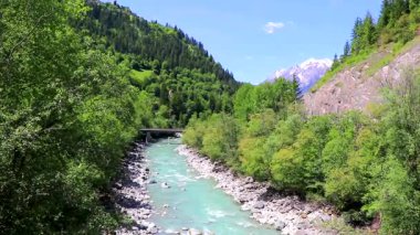 Turkuaz mavi ve yeşil nehir buharı ve taşlı şelale hanı. Çimen ağaçları ve Alpler 'deki dağ manzarası. Landeck Tyrol Avusturya..