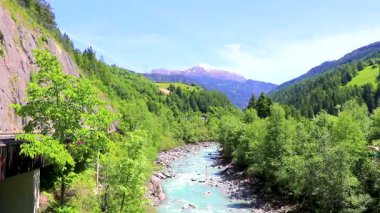 Turkuaz mavi ve yeşil nehir buharı ve taşlı şelale hanı. Çimen ağaçları ve Alpler 'deki dağ manzarası. Landeck Tyrol Avusturya..