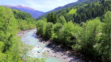 Turkuaz mavi ve yeşil nehir buharı ve taşlı şelale hanı. Çimen ağaçları ve Alpler 'deki dağ manzarası. Landeck Tyrol Avusturya..