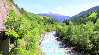 Turkuaz mavi ve yeşil nehir buharı ve taşlı şelale hanı. Çimen ağaçları ve Alpler 'deki dağ manzarası. Landeck Tyrol Avusturya..