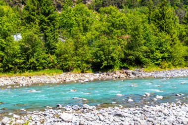 Turkuaz mavi ve yeşil nehir buharı ve taşlı şelale hanı. Çimen ağaçları ve Alpler 'deki dağ manzarası. Uçamayan Landeck Tyrol Avusturya..