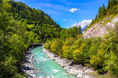 Turkuaz mavi ve yeşil nehir buharı ve taşlı şelale hanı. Çimen ağaçları ve Alpler 'deki dağ manzarası. Uçamayan Landeck Tyrol Avusturya..
