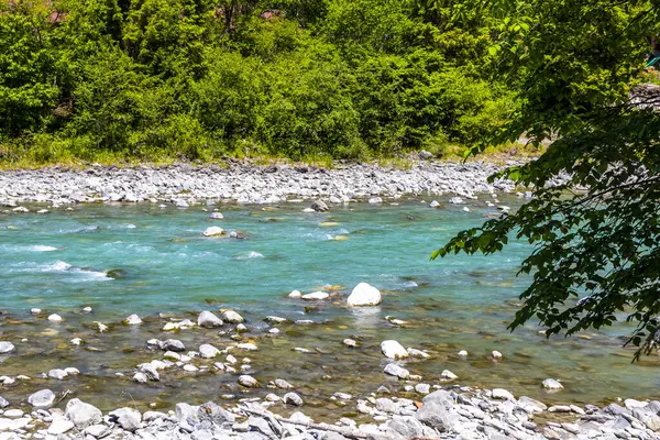 Turkuaz mavi ve yeşil nehir buharı ve taşlı şelale hanı. Çimen ağaçları ve Alpler 'deki dağ manzarası. Uçamayan Landeck Tyrol Avusturya..