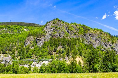 Dağ ve dağlık arazi dağları kayalar ve tepeler yeşil çayırlar köy ormanı köknar ağaçları ve bulutlu mavi gökyüzü Fliess Landeck Tyrol Avusturya.