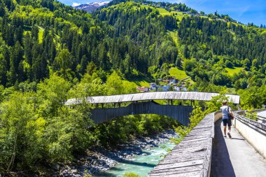 Turkuaz mavi ve yeşil nehir buharlı ahşap köprü ve taşlı şelale hanı. Çimen ağaçları, doğa ve dağ manzarası Alplerde uçuşan Landeck Tyrol Austria..