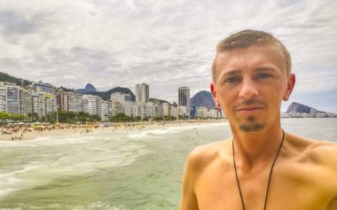 Yakışıklı erkek turist, Rio de Janeiro Eyaleti Rio de Janeiro Brezilya 'da Copacabana Sahili Tropikal Bahçesinde Mavi Turkuaz Palmiye Ağaçları ve Beyaz Kumsal Kumu ile selfie çekiyor..