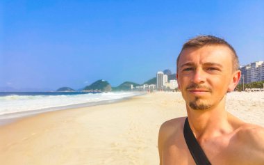 Yakışıklı erkek turist, Rio de Janeiro Eyaleti Rio de Janeiro Brezilya 'da Copacabana Sahili Tropikal Bahçesinde Mavi Turkuaz Palmiye Ağaçları ve Beyaz Kumsal Kumu ile selfie çekiyor..
