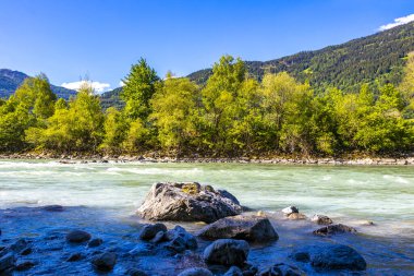 Turkuaz mavi ve yeşil nehir buharı ve taşlı şelale hanı Alpler Zams Landeck Tyrol Avusturya 'daki dağlar arasındaki çimen ağaçları..