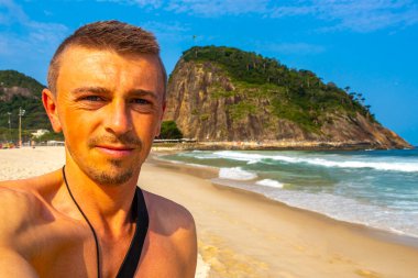 Yakışıklı erkek turist, Rio de Janeiro Eyaleti Rio de Janeiro Brezilya 'da Copacabana Sahili Tropikal Bahçesinde Mavi Turkuaz Palmiye Ağaçları ve Beyaz Kumsal Kumu ile selfie çekiyor..