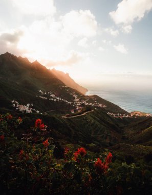 Beautiful landscape shot of coastline with hills and ocean on background in Canary Islands - Tenerife. Sunset over the mountain peaks and village with serpentines -  northern part of Tenerife.